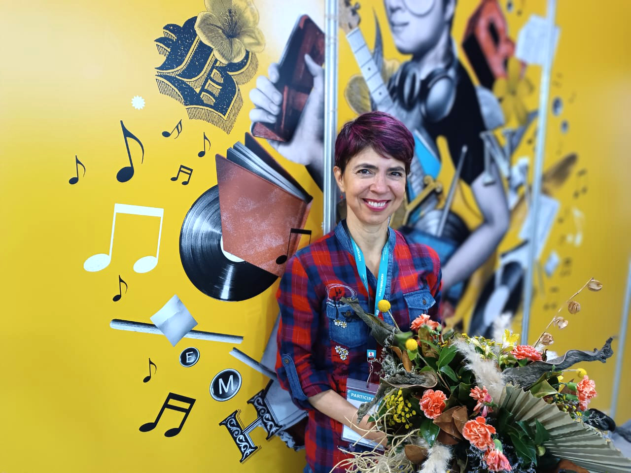 Teresa González Arce sostiene unas flores delante de un mural de la FIL Guadalajara 2022